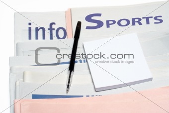 Note and pen, over stacked sports newspapers