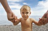 portrait of a baby boy holding his father's hands on beach backg