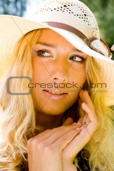 Young blond woman in a hat smiling in a park