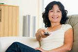 Woman sitting in living room holding remote control smiling