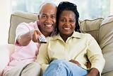 Couple relaxing in living room holding remote control and smilin