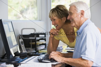 Couple in home office with computer and paperwork smiling