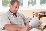 Man in living room reading newspaper smiling