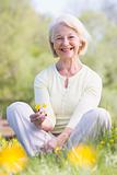 Woman sitting outdoors smiling and holding a Buttercup flower