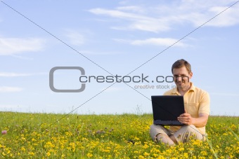 Man sitting with laptop computer in a meadow