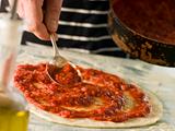 Spooning Tomato sauce onto a Pizza Base