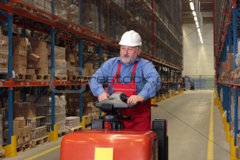A senior worker driving the fork lift through a storage room in a factory