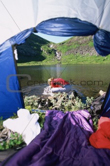 Woman washing face in lake,  view through tent entrance