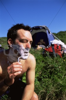 Man shaving in the outdoors next to tent