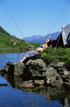 Young woman sunbathing on rocks next to lake