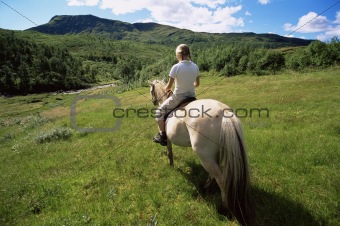Rear view of young woman riding horse in rural setting
