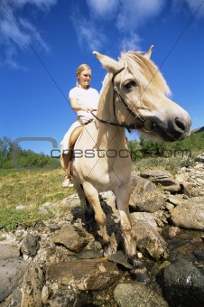 Young woman crossing a river by horse