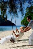 Man swinging woman on swing at beach, 