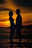 Silhouette of couple standing face to face on beach at sunset