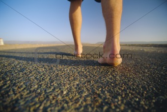 Rear view of man walking along road, low section