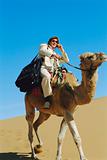 Man with mobile phone riding camel in desert