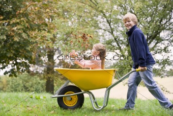 Young boy pushing girl in wheelbarrow
