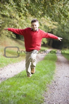 Young boy running along woodland path