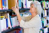 Senior woman pulling a library book off shelf