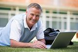 Man using laptop while lying in grass on campus