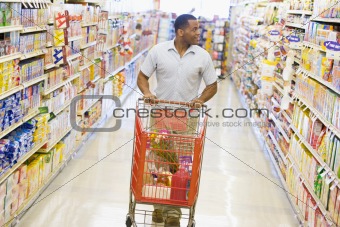 Man pushing trolley along supermarket aisle
