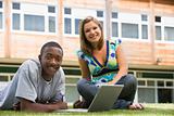 Two college students using laptop on campus lawn, 