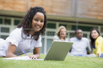 Young woman using laptop on campus lawn, with other students rel