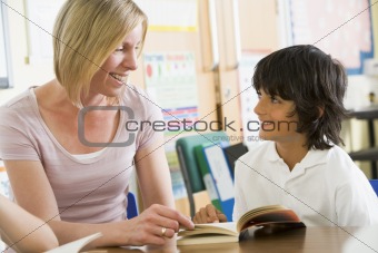 A schoolboy and his teacher reading a book in class