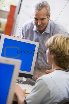 A teacher talks to a schoolboy using a computer in a high school