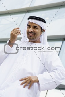 A Middle Eastern businessman standing outside an office block ta