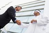 A Middle Eastern businessman and Caucasian man shaking hands out