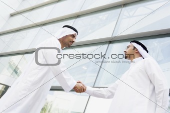 Two Middle Eastern businessmen shaking hands outside an office b