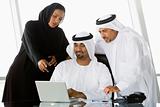 Two Middle Eastern businessmen and a woman beside a laptop