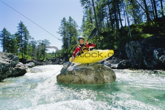 Kayaker perched on boulder in river