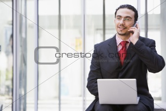 Businessman using laptop and mobile phone outside