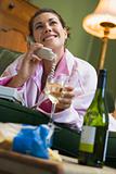 A young woman in her pyjamas on the phone and drinking wine