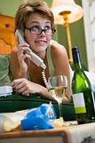 A young woman in her pyjamas on the phone and drinking wine