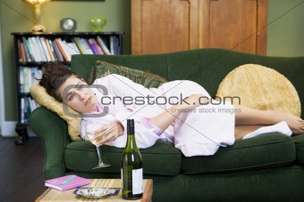 A young woman lying on her couch drinking wine