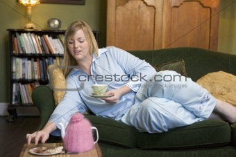 A young woman lying on her couch drinking tea
