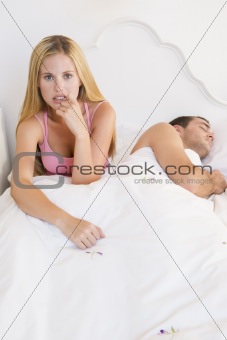 A young couple in bed with the woman looking anxious
