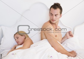 A young couple in bed with the man looking worried