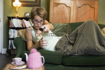 A young woman lying on her couch watching television