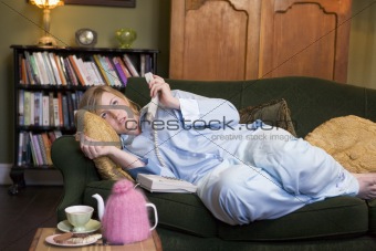 A young woman lying on her couch talking on the phone