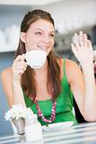 A young woman sitting in a cafe drinking tea and waving