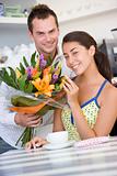 A young man giving flowers to a young woman in a cafe