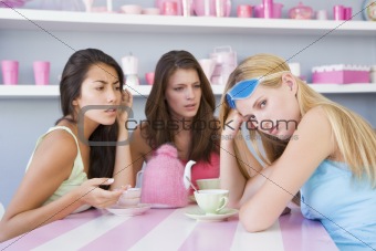 Two young women enjoying a tea party while one sits apart wearing a gel eye mask