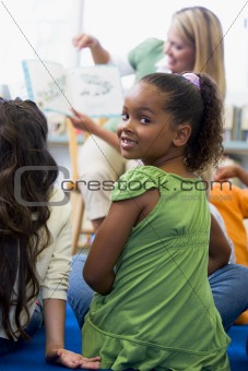 Kindergarten teacher reading to children in library, girl lookin