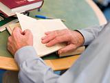 Close-up of mature student's hands turning book page in library