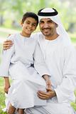 A Middle Eastern man and his son sitting in a park