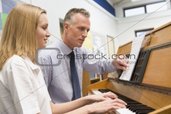 Teacher with schoolgirl playing piano in music class